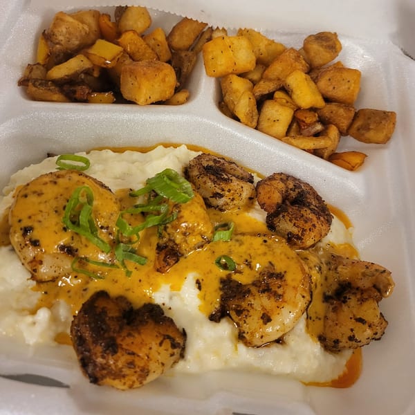 Southern Fusion Bistro's shrimp and grits with a side of seasoned breakfast potatoes in a takeout container.