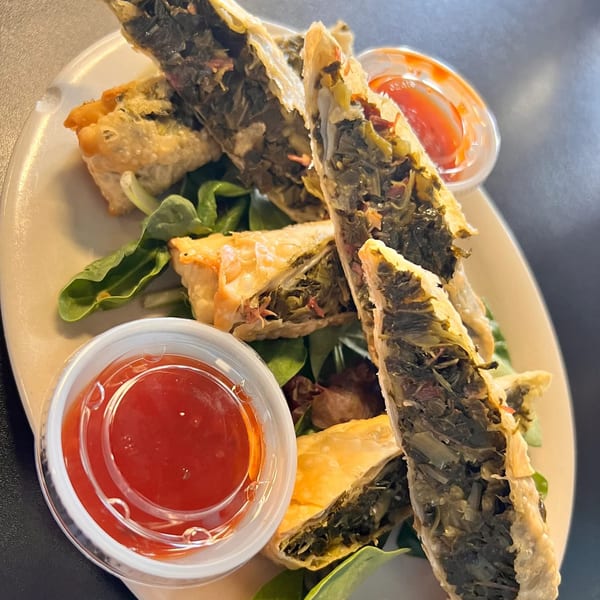 Crispy Southern Fusion Bistro collard green egg rolls with dipping sauce on a white plate.
