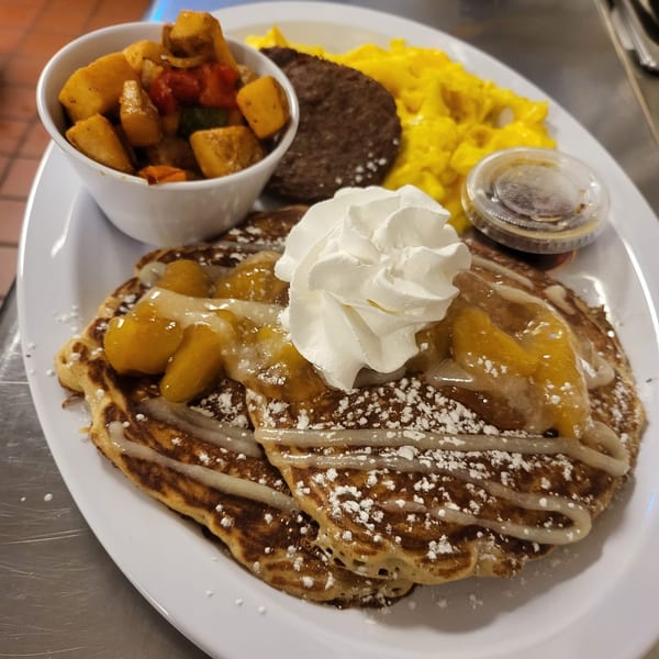 Southern Fusion Bistro's breakfast plate with pancakes, peaches, whipped cream, scrambled eggs, sausage, and potatoes.